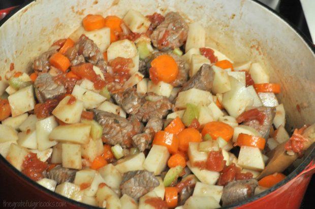 Potatoes, carrots, tomatoes are added to beef stew meat in pan.